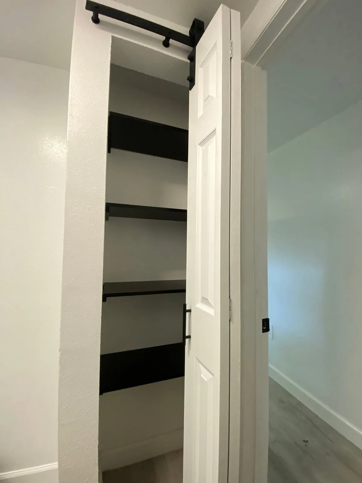 White closet shelves visible behind an open sliding door with black hardware.