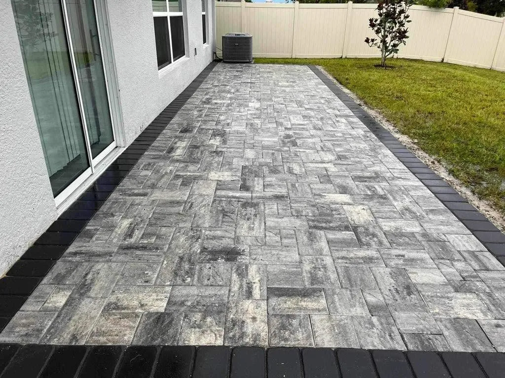 Rectangular gray paver patio with a dark border beside a house.