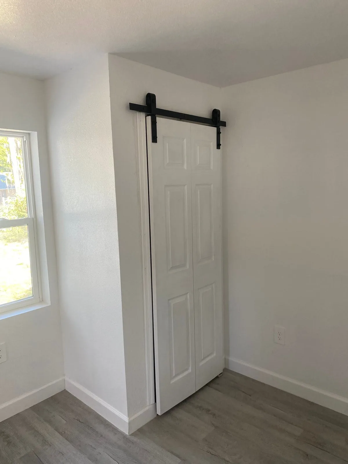White paneled sliding interior door on a black rail beside a window.